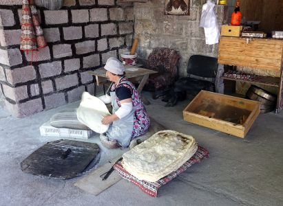 Paní připravuje placky pečené v podzemní peci.